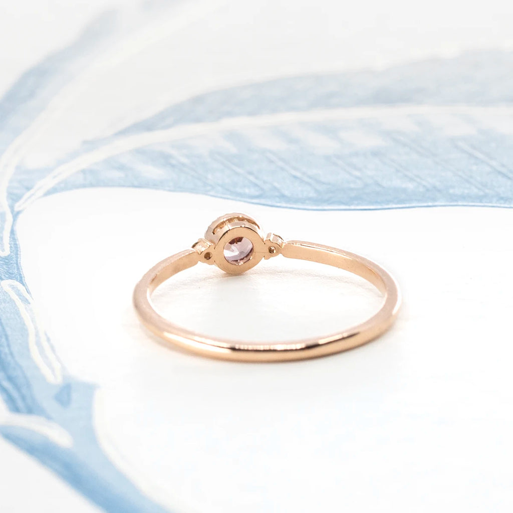Back view of a rose gold 18 karat engagement ring featuring a central dark rose gemstone. The bridal ring is seen photographed on an artistic background. It is available at independent Canadian jewelry store Ruby Mardi.