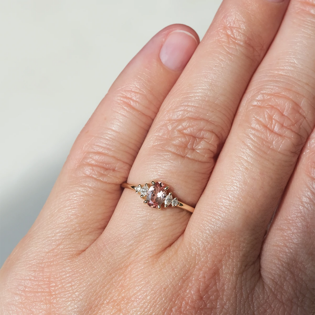 Malaya garnet and diamond engagement ring worn on hand, featuring a pink center stone and tapered marquise and round diamonds, set in yellow gold by Maksym, available at Ruby Mardi, Montreal jewelry store.