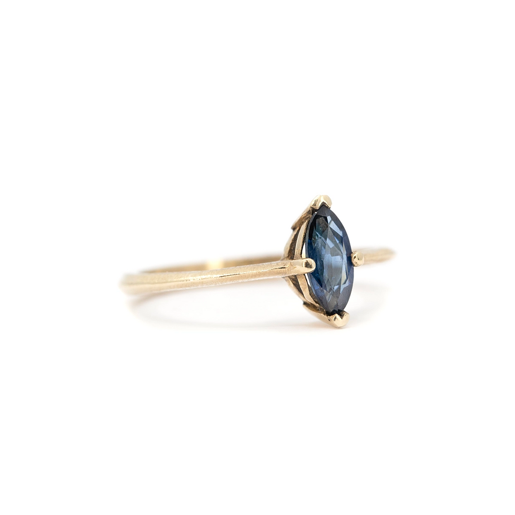 Side view of marquise blue sapphire solitaire ring with knife-edge yellow gold band and textured finish, minimalist fine jewelry by Ruby Mardi.