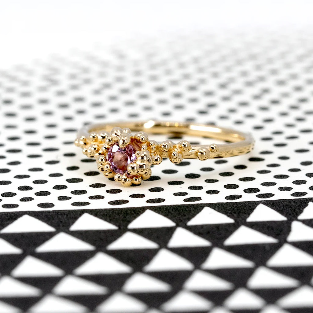 Gold ring with a central purple sapphire surrounded by organic bead detailing, designed by Meg Lizabet for the Baleal Signature Collection. Photographed on a bold black-and-white geometric background. Handcrafted in Montreal, Canada.