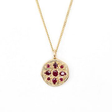 An organic handmade gold pendant medaillion with gold granules and encapsulated rubies seen on a white background. Find this beautiful piece of fine jewelry by Meg Lizabet at Ruby Mardi, a high end jewelry store located in Montreal's Little Italy.