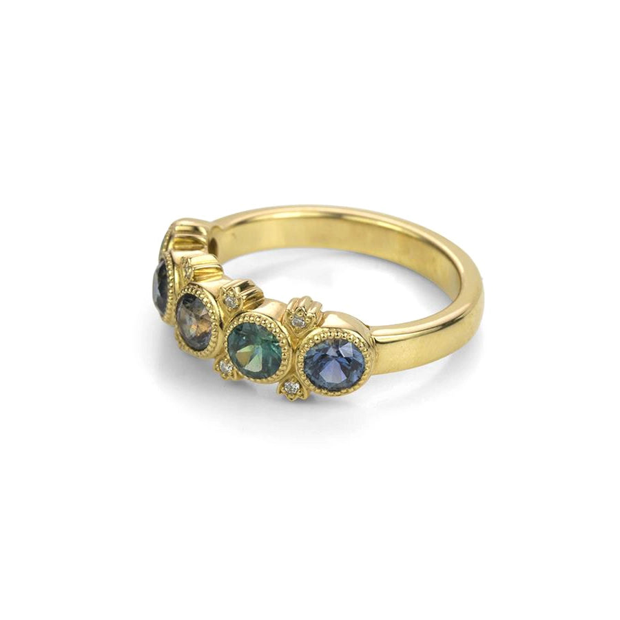 The top view of the Grace ring from Bramston Goldsmithing features a yellow gold half eternity band with teal sapphire and small diamonds. This high-end bridal jewelry is presented at the Ruby Mardi jewelry store, the only jewelry gallery from Canadian jewelers in Montreal.