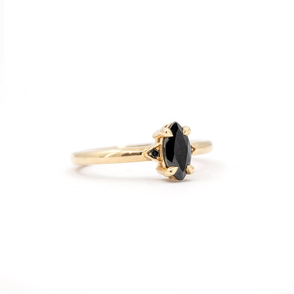 Yellow gold solitaire ring featuring a marquise black gemstone, flanked by small black diamond accents, by Canadian jeweller Liane Vaz.