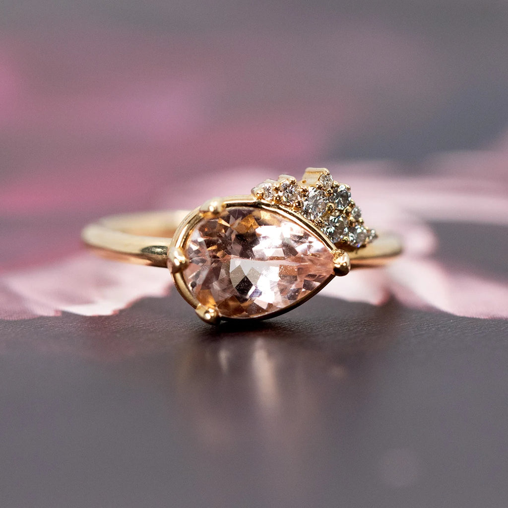 Pear-shaped morganite engagement ring with a shimmering diamond cluster, set in 14k yellow gold. Handcrafted in Montreal by Sheena Purcell, available at Ruby Mardi, the best jewelry store in Canada. 