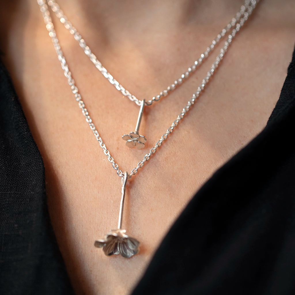 Layered white gold wildflower pendants worn together, featuring the small myosotis forget me not pendant by Fleurs Sauvages Qc. Nature inspired designer jewelry from Ruby Mardi Montreal.