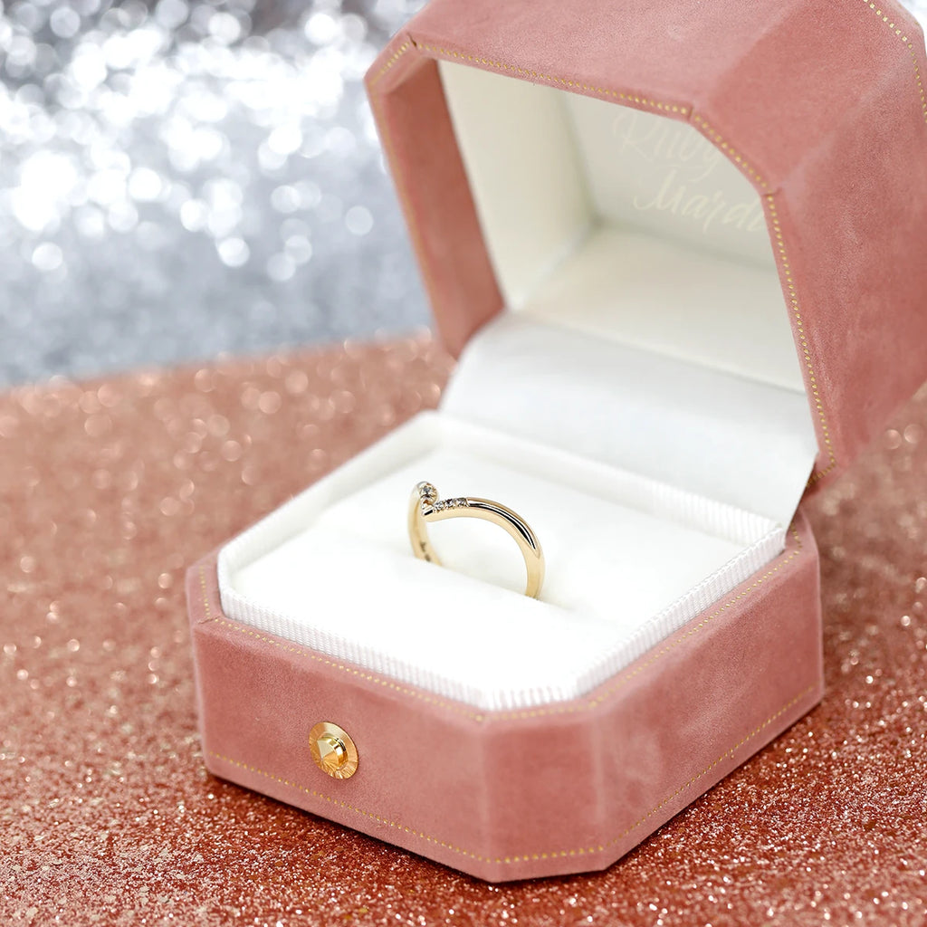Close up of a diamond wedding band on a pink velvet box and a pink glitter background. 