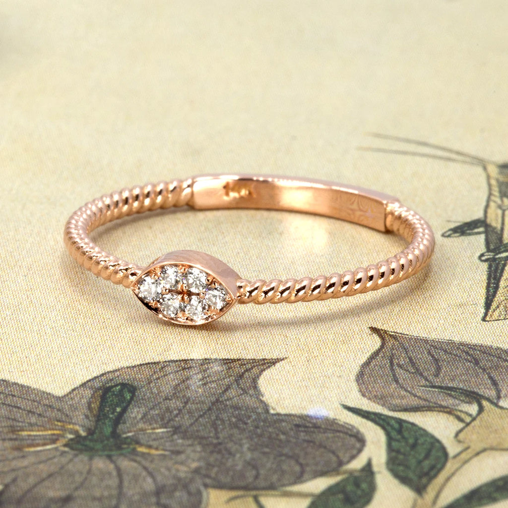 Minimalist rose gold ring with twisted band and marquise-shaped cluster of natural white diamonds, designed by Oleg Leybman. Photographed on a vintage floral background. Available at Ruby Mardi in Montreal.
