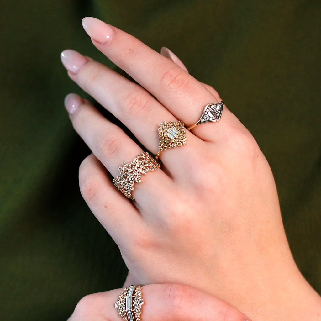 Close-up view of an array of exquisite high-end rings, including an elegant alternative bridal ring in yellow gold, worn on the delicate hands of a woman with long nude nails. The collection features six stunning rings from designer Oleg Leybman, each adorned with intricate designs and sparkling natural diamonds, exuding an oriental vibe. The luxurious ensemble of rings showcases a remarkable blend of artistry and sophistication, perfect for making a bold statement.
