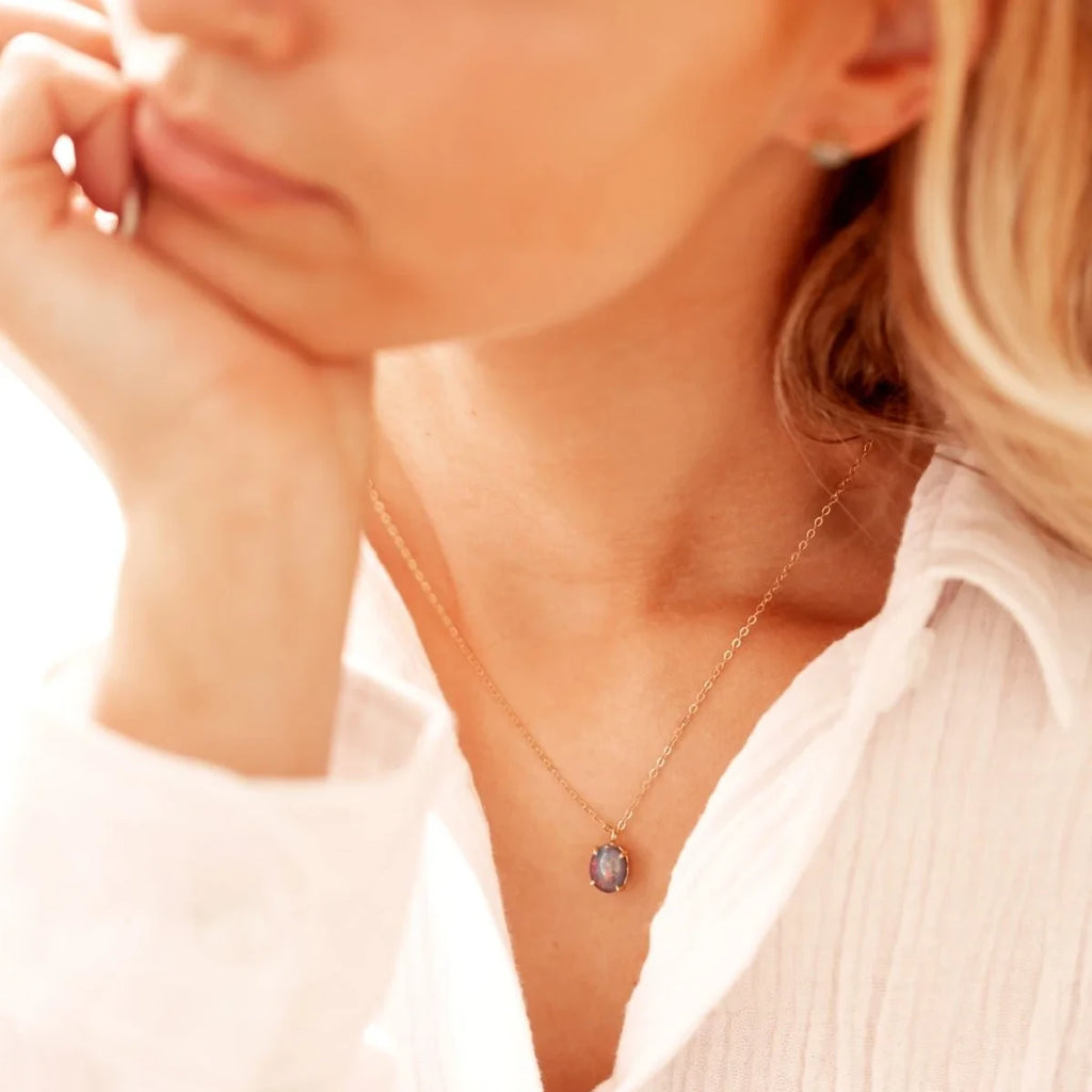 Woman wearing oval opal stud earrings in 14k yellow gold with a delicate floral design.