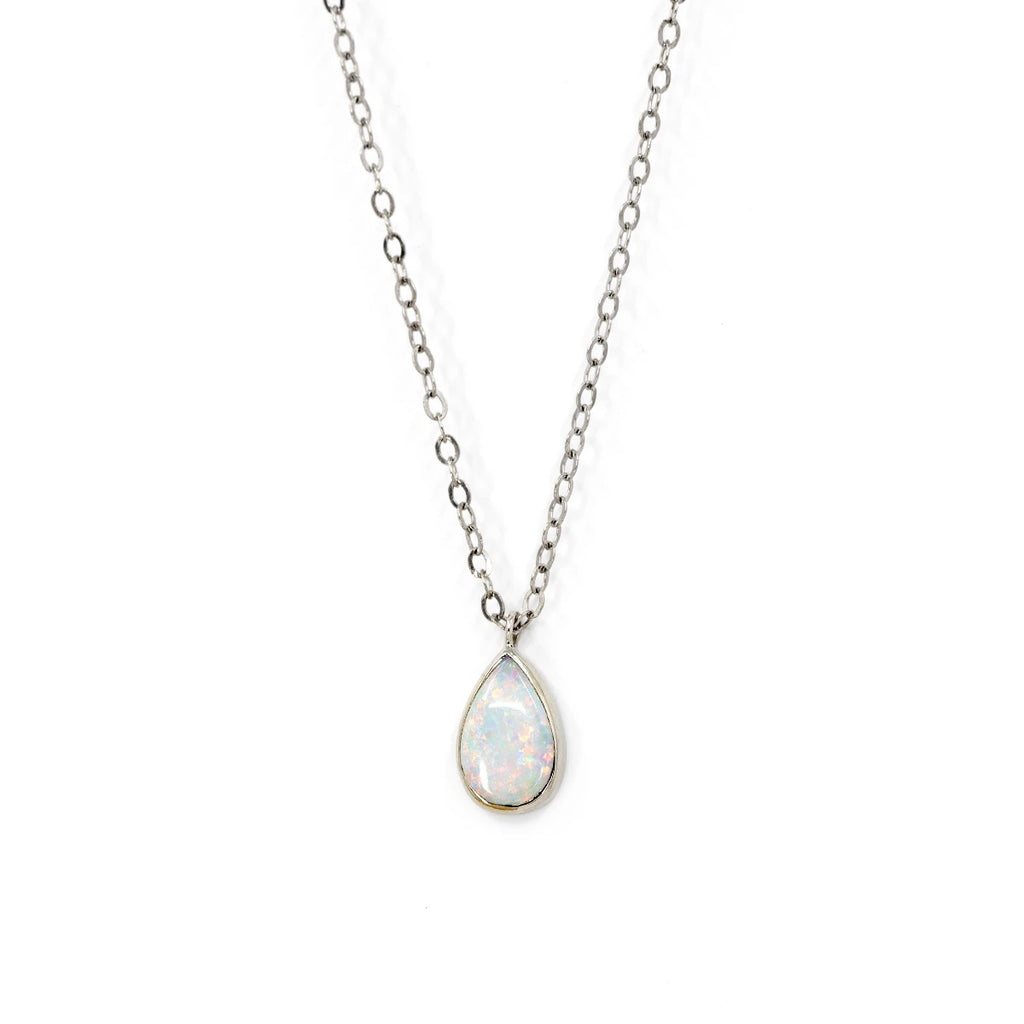 Classic piece of jewelry in white gold featuring a pear shape white opal with a play-of-color of green, pink, and blue. This gold pendant is seen photographed on a white background. A jewel handmade in Toronto by Rooz Jewellery brand, and available at the Montreal jewelry store Ruby Mardi, in Little Italy. 