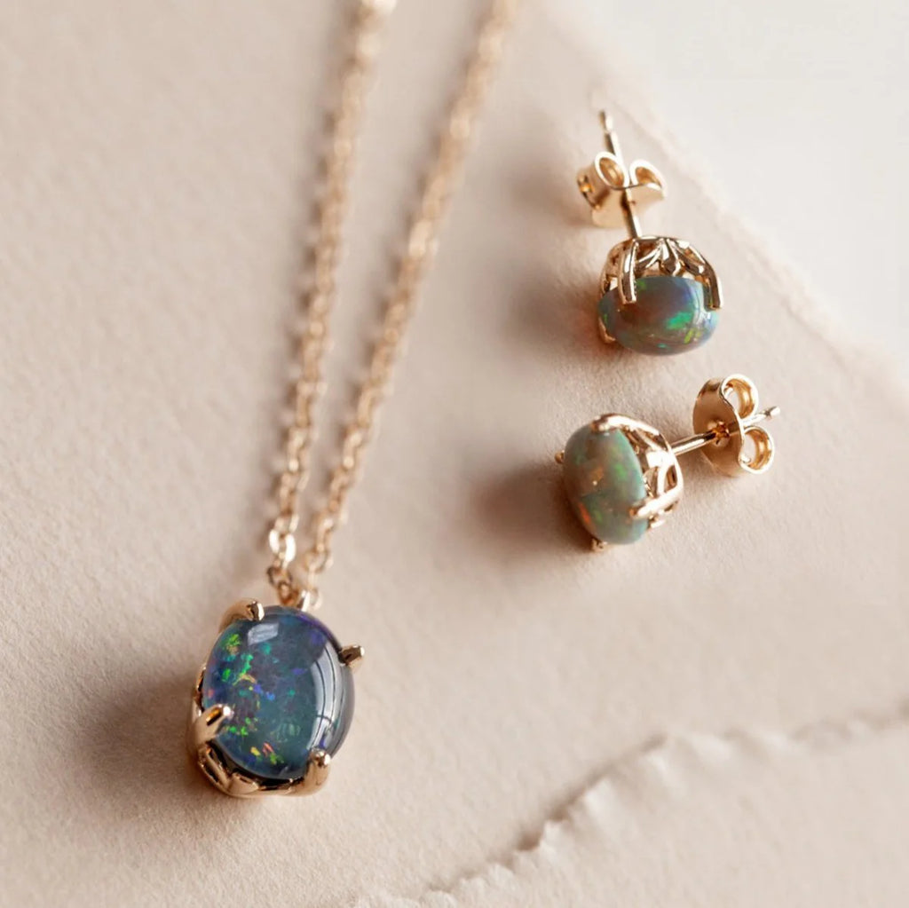 Australian opal necklace and matching stud earrings with gold floral settings displayed on neutral paper background.