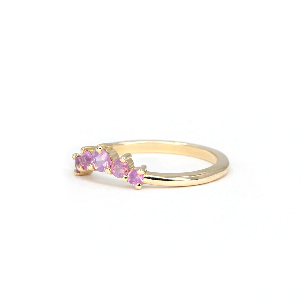 Opalescent pink sapphire contour ring with five round sapphires set in shared prongs on a polished 14k yellow gold band. Handmade by Emily Gill, available at Ruby Mardi, Montreal.

