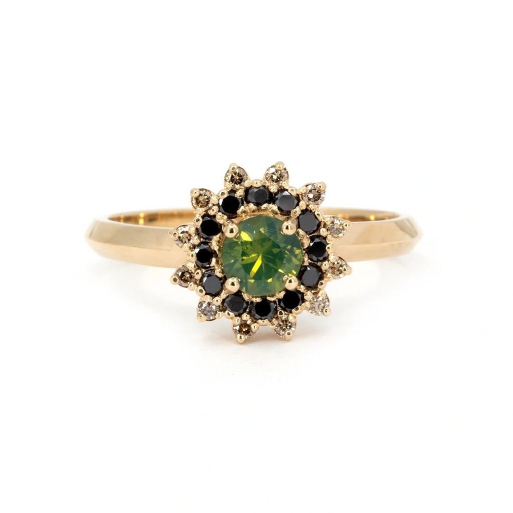 Close-up of a yellow gold ring featuring a round opalescent green sapphire, encircled by a striking starburst halo of alternating black and white diamonds. Designed and handmade in Montreal by Ruby Mardi.