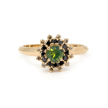 Close-up of a yellow gold ring featuring a round opalescent green sapphire, encircled by a striking starburst halo of alternating black and white diamonds. Designed and handmade in Montreal by Ruby Mardi.