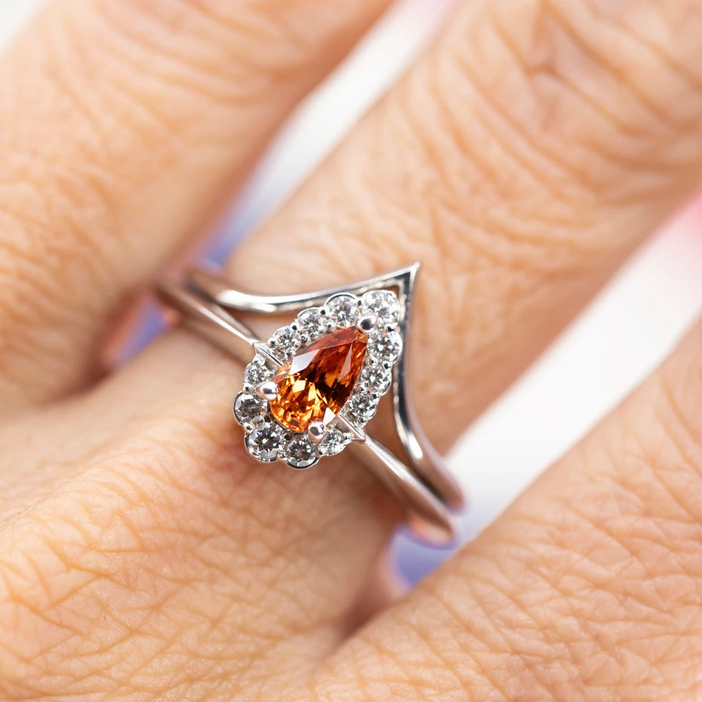 White gold engagement ring with stunning spessartite garnet and diamond halo, created by Ruby Mardi, a fine jewelry store located in Montreal's Little Italy. The bridal ring is seen with its matching crown wedding band for a beautiful and perfect match.