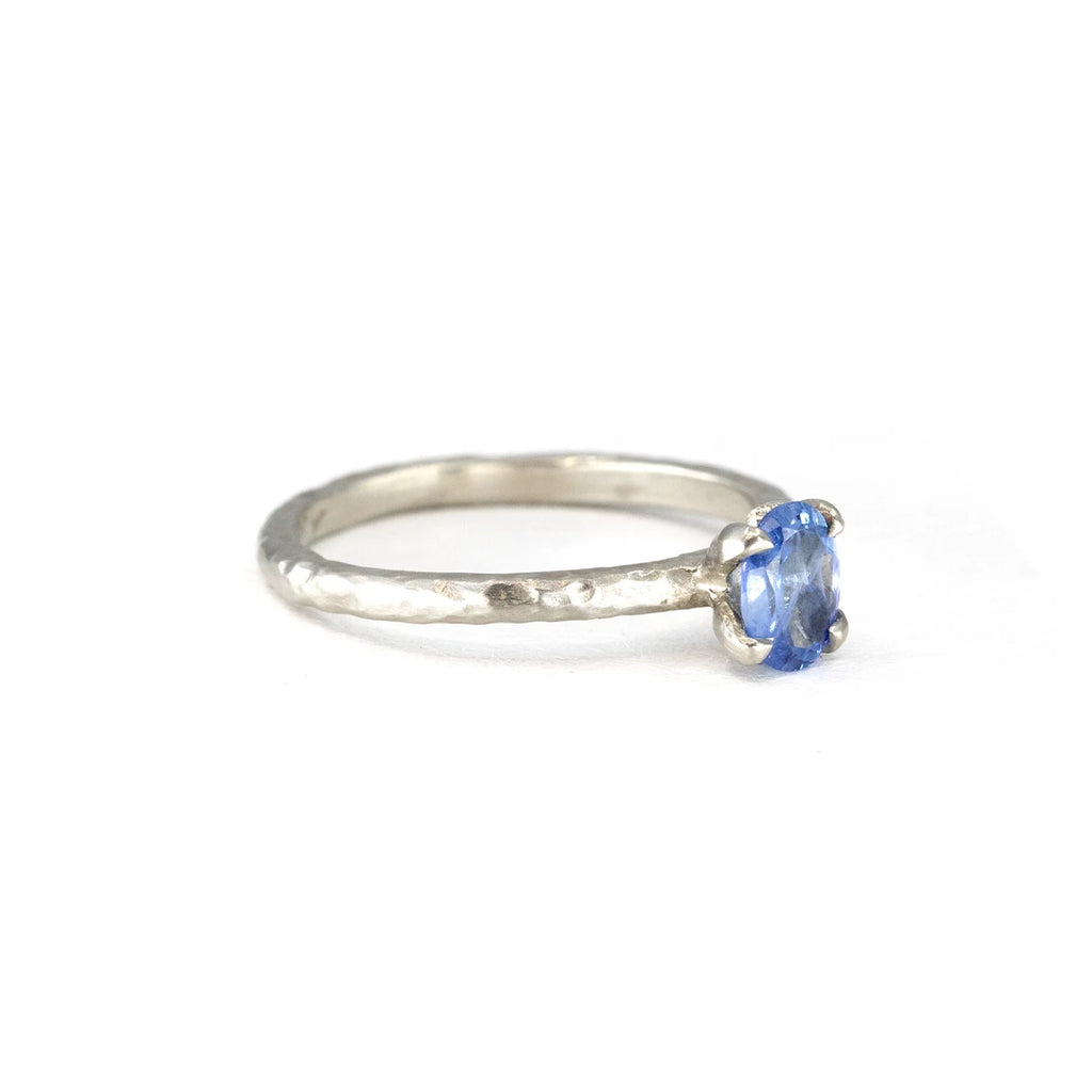 A side view of an elegant white gold engagement ring featuring a textured band and a shimmering oval blue sapphire. Handmade by Anouk Jewelry, available exclusively in Montreal at Ruby Mardi.







