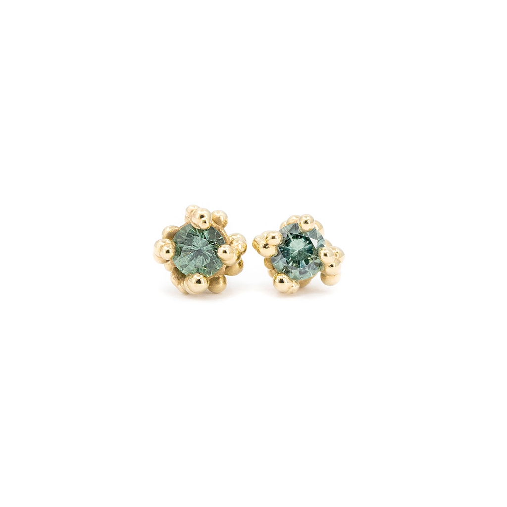 Organic stud earrings handcrafted in 14k yellow gold by Meg Lizabet, featuring round light teal sapphires set in a unique beaded setting. Fine jewelry available exclusively at Ruby Mardi in Montreal, Canada.