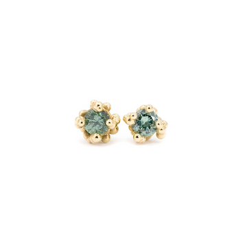 Organic stud earrings handcrafted in 14k yellow gold by Meg Lizabet, featuring round light teal sapphires set in a unique beaded setting. Fine jewelry available exclusively at Ruby Mardi in Montreal, Canada.