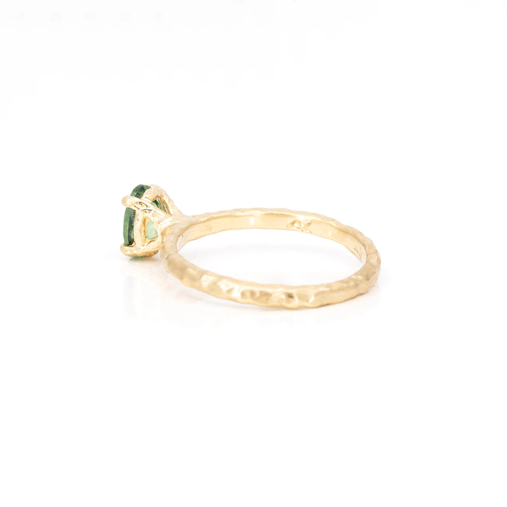 A yellow gold ring with a textured band is seen from the side. It's a solitaire engagement ring featuring a green sapphire.