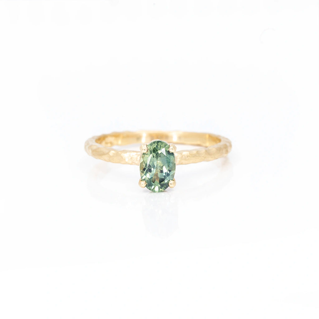 Front view on a white background of a solitaire gold ring featuring an oval green with yellow hues sapphire. It's an handmade ring with an organic and natural vibe. It was handmade in Toronto by Anouk Jewelry and is available in Montreal at jewelry store Ruby Mardi.