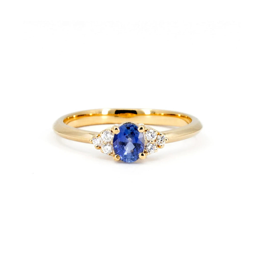 Classic engagement ring with a central oval blue sapphire and three natural diamonds on both sides, set in 14k yellow gold, seen photographed on a white background.