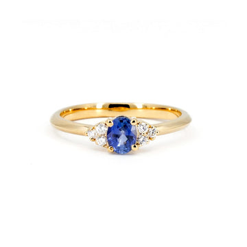 Classic engagement ring with a central oval blue sapphire and three natural diamonds on both sides, set in 14k yellow gold, seen photographed on a white background.
