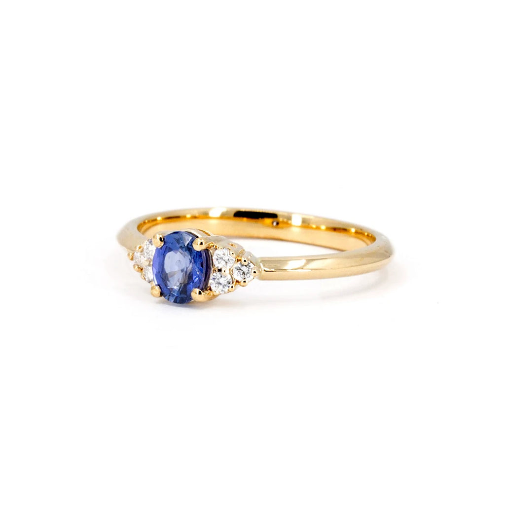 Half side view of a classic yellow gold engagement ring with a royal blue sapphire and natural diamonds, seen photographed on a white background. The ring was handcrafted in Montreal by local jewelry store Ruby Mardi.