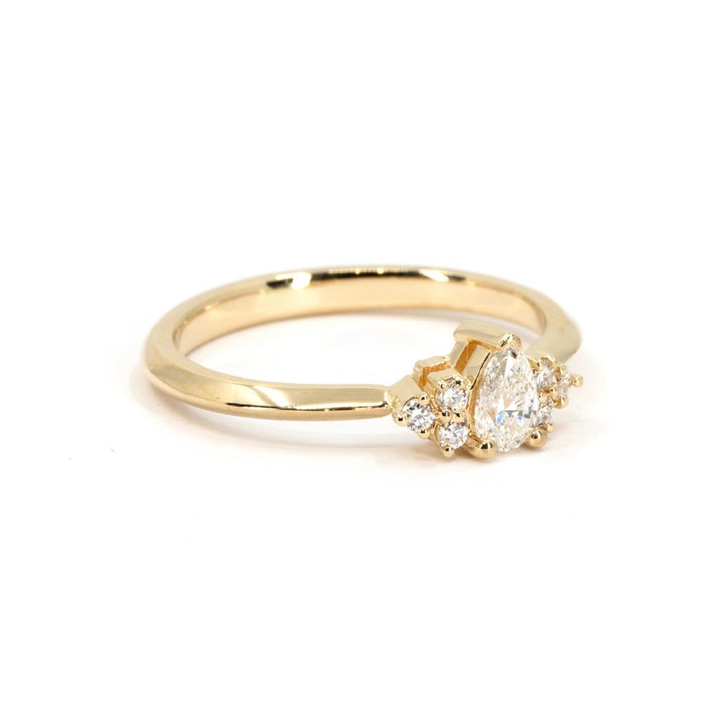 Side view of a yellow gold engagement ring featuring a pear-shaped center diamond with clustered round diamond accents. Handcrafted by Ruby Mardi in Montreal.