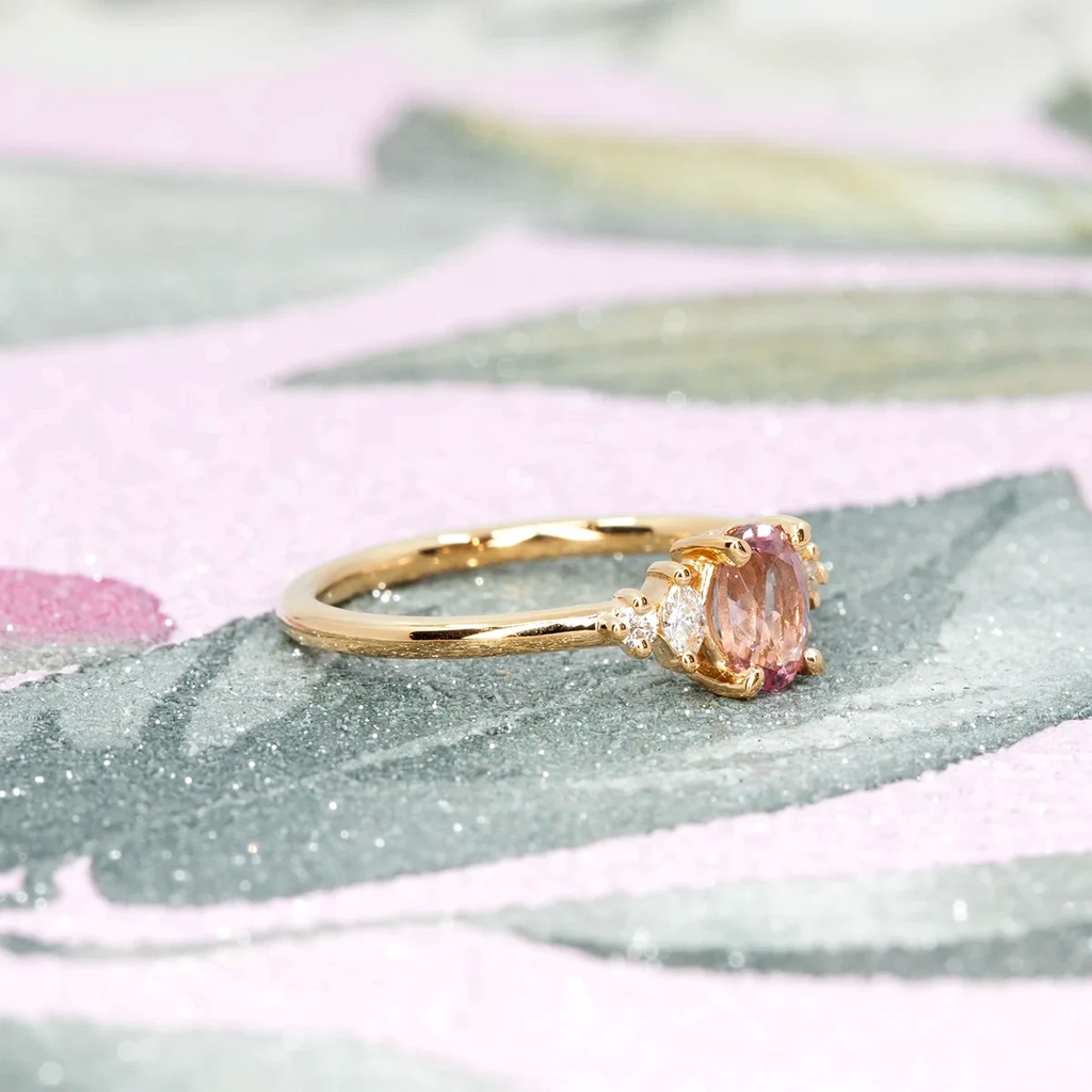 Side view of a Malaya garnet and diamond engagement ring in yellow gold, handmade by Maksym for Ruby Mardi in Montreal. Shown on a floral textured background.