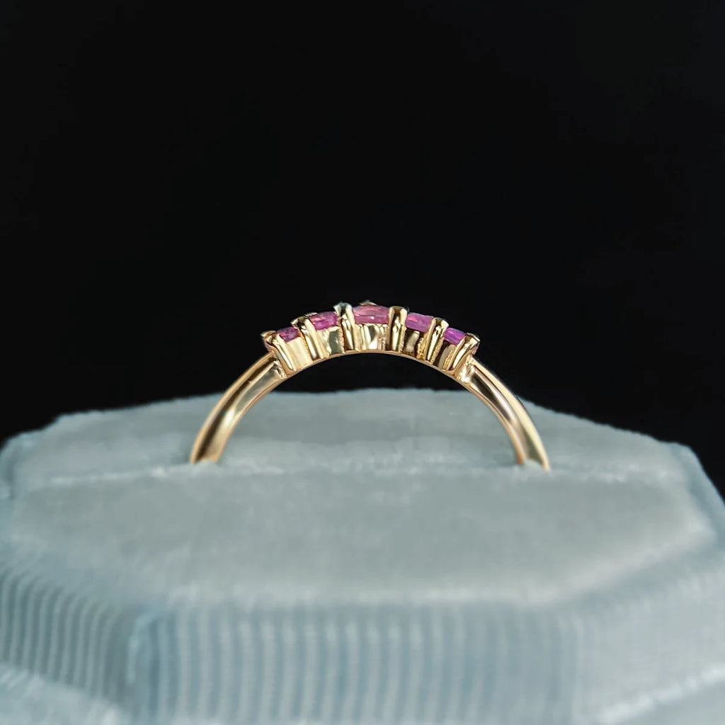 Pink sapphire contour band in 14k yellow gold, featuring five heat-treated baguette-cut sapphires in a curved setting. Shown on a pale velvet ring box with a dark background. Fine handmade jewelry available at Ruby Mardi, Montreal.