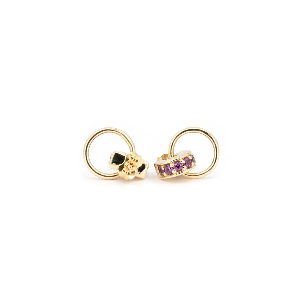Purple gemstone door knocker stud earrings in yellow gold made by Meg Lizabet, designer jewelry from Montreal, Canada. The pair features round purple garnets set in a curved band with a dangling gold hoop, photographed on white background.