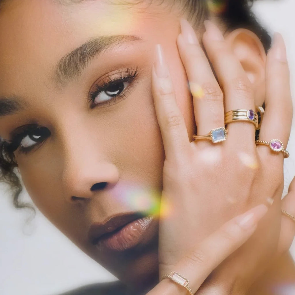 Portrait of a model wearing multiple gold rings, including the Raspberry Jam ring with pink sapphire and twisted band by In the Light of Day Jewelry, available at Ruby Mardi in Montreal.