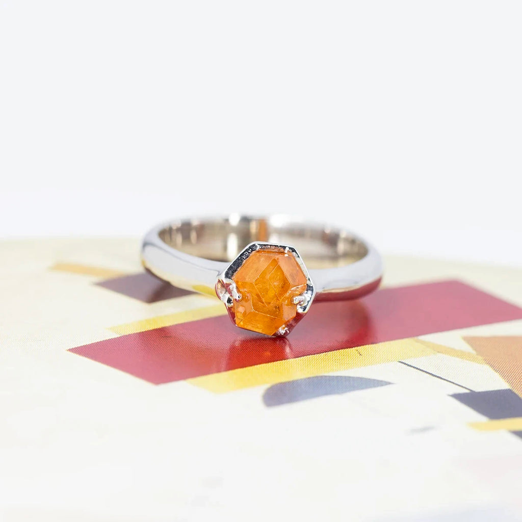 Front view on a colored background of a bold white gold ring with a raw orange gemstone from Nigeria. This gender neutral alternative engagement ring was made in Montreal by jewelry designer François Charest, and is only available at fine jewellery store Ruby Mardi, in Little Italy.