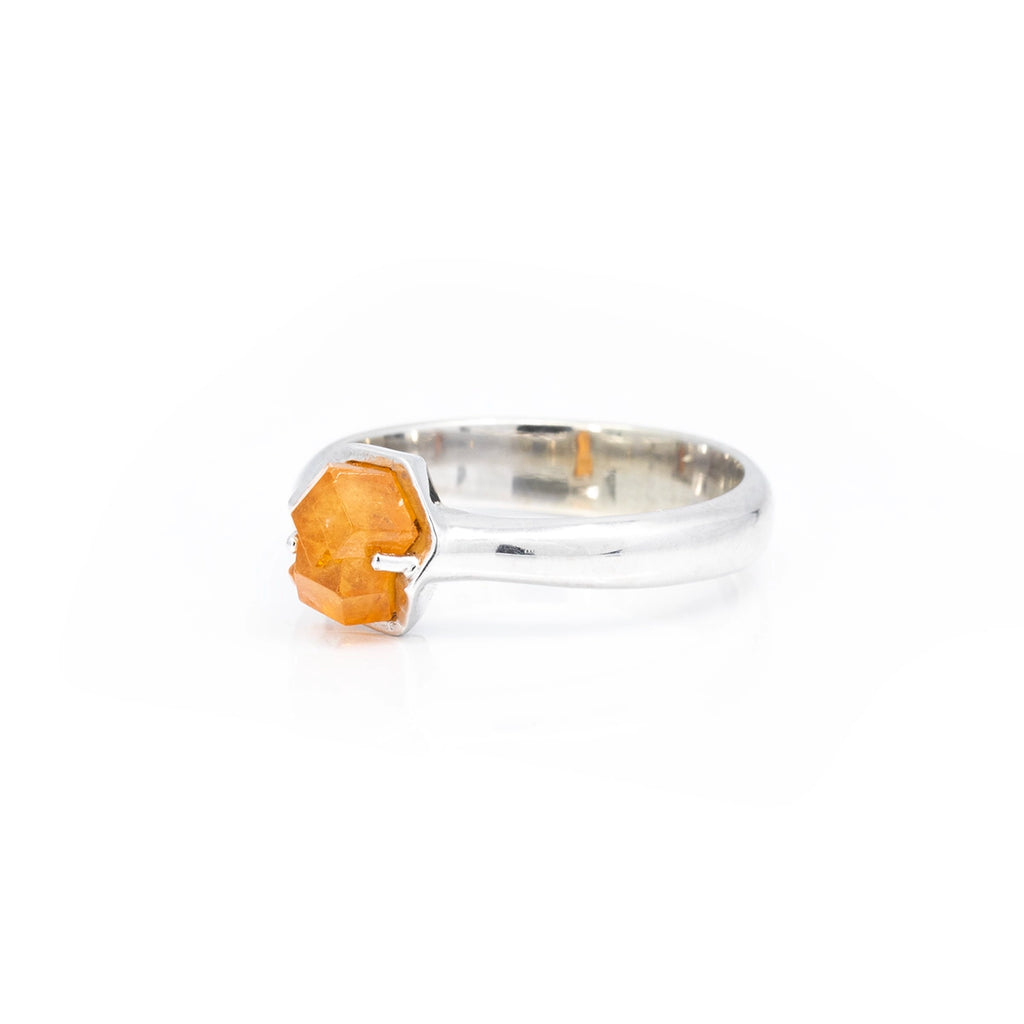 Side view on a white background of a thick white gold ring with a raw orange garnet from Nigeria. This gender fluid piece of jewelry was handmade and designed in Montreal by independent jeweller François Charest, and is only available at fine jewelry store Ruby Mardi.