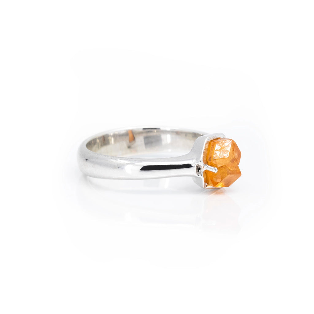 Side view on a white background of a bold white gold ring featuring a raw orange garnet. This statement ring was handmade in Montreal by a young independent artist and is only available at jewelry store Ruby Mardi.
