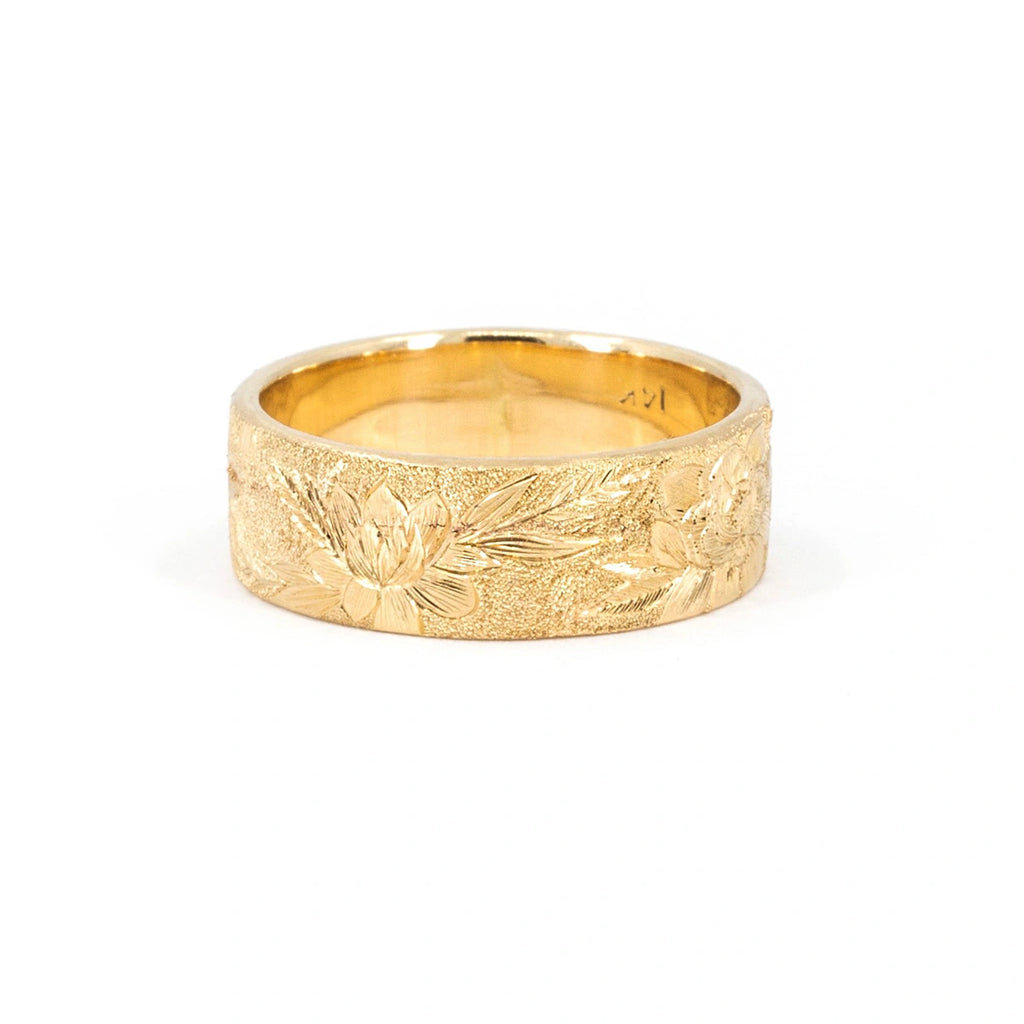 Thick, wide 14-carat yellow gold band featuring finely hand-engraved flowers and a sandblasted texture. The fine jewelry is photographed against a white background. It was created by independent brand Rebel & Rogue. This is a unique piece of bridal jewelry only available at Ruby Mardi.