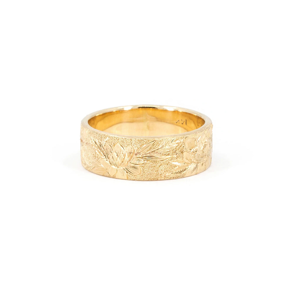 Thick, wide 14-carat yellow gold band featuring finely hand-engraved flowers and a sandblasted texture. The fine jewelry is photographed against a white background. It was created by independent brand Rebel & Rogue. This is a unique piece of bridal jewelry only available at Ruby Mardi.