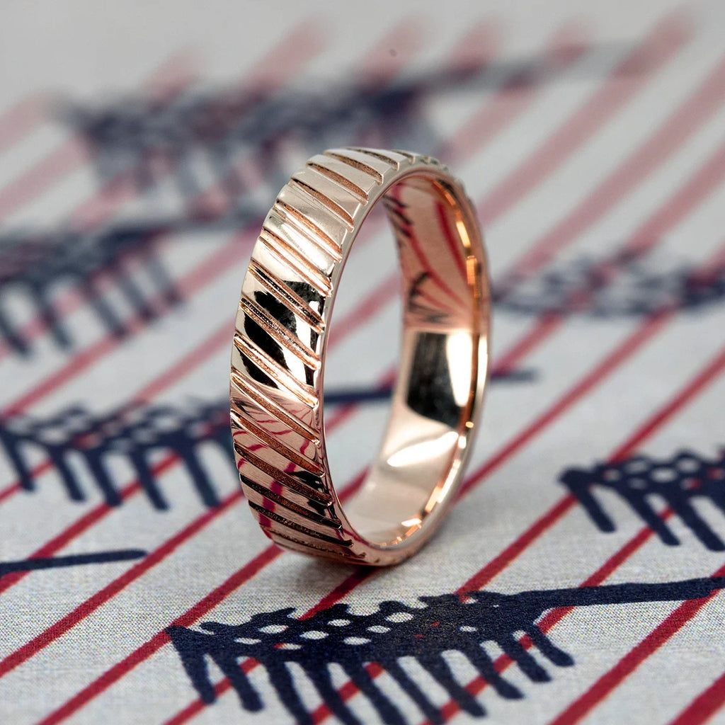 Rose gold Strata wedding band featuring raised diagonal lines and a polished surface. Contemporary men’s ring photographed on a patterned textile, made in Montreal.