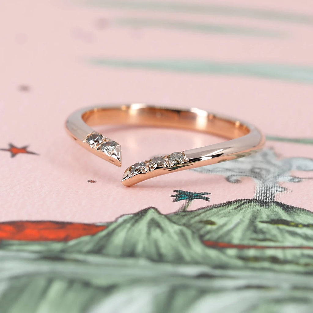 Open tilted rose gold wedding band with champagne diamonds seen photographed on a pink background. This bridal ring is handmade in Montreal by local independent jewelry store Ruby Mardi.