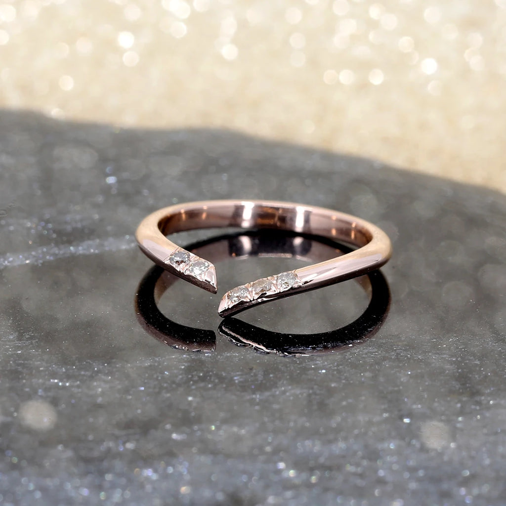 A twisted open wedding band in rose gold set with 5 natural golden brown diamonds. The wedding ring is shown photographed on a black marble and a sparkling background.