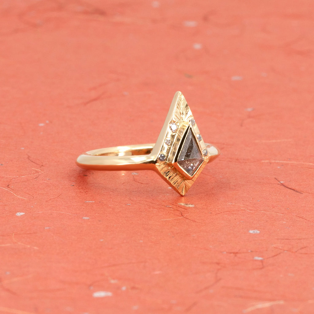 Unique alternative engagement ring in yellow gold, with a central salt-and-pepper kite-shaped diamond and diamond accents seen photographed on a orange-red Japanese paper. Handcrafted by independent Canadian brand Rebel & Rogue. Available at Ruby Mardi, the coolest jewelry store in Canada.