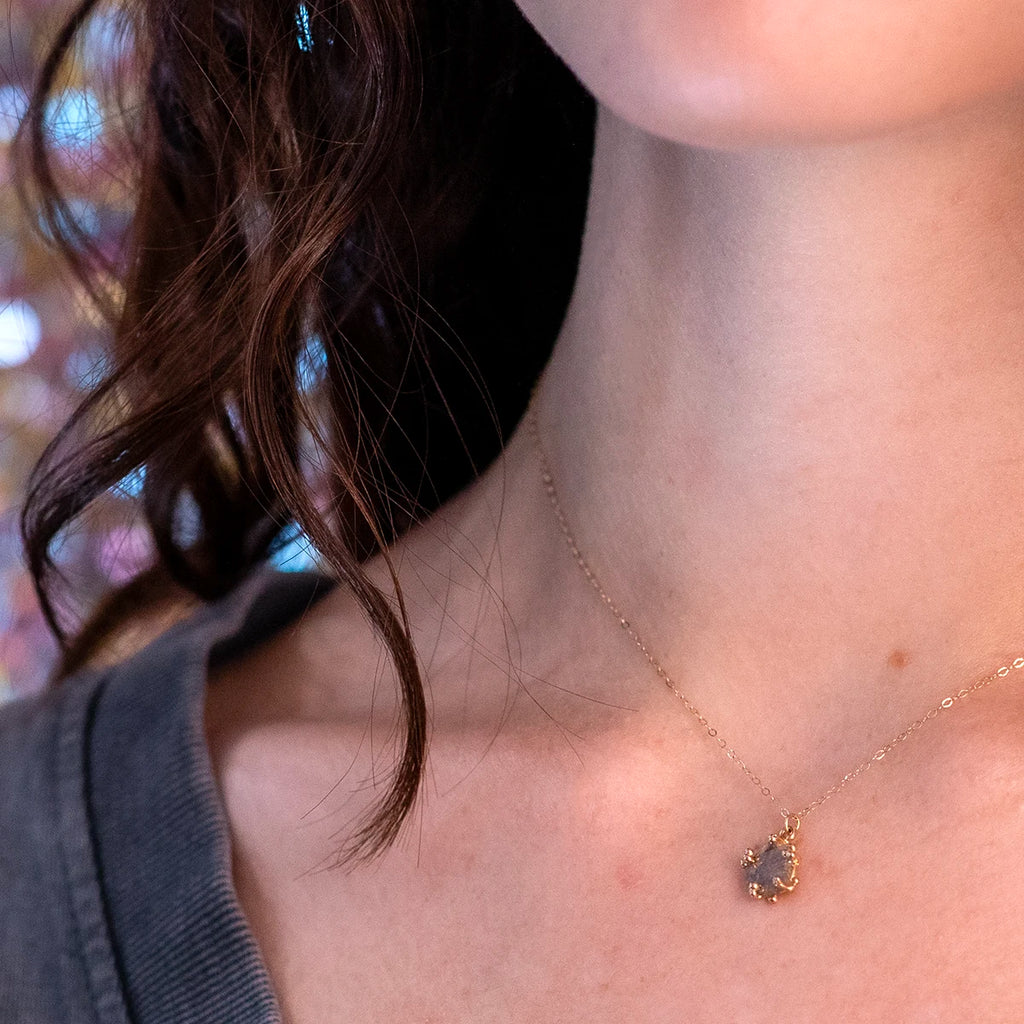 Close-up of a young woman with long, wavy hair wearing a V-neck t-shirt that beautifully showcases the salt & pepper diamond pendant necklace. The colorful, sparkling background adds a festive touch, reflecting the vibrant spirit of Ruby Mardi.