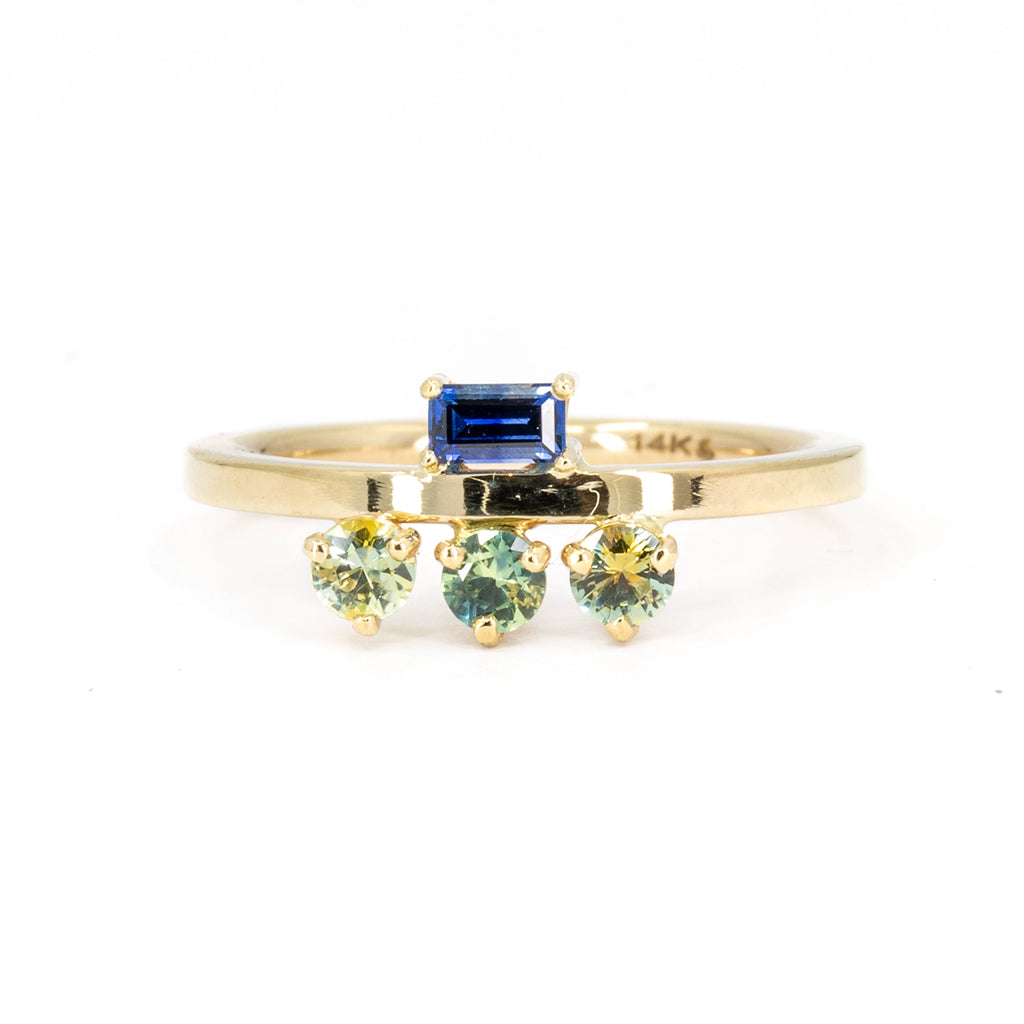 One-of-a-kind engagement ring or right hand ring of a funky style designed by American indie brand In the Light of Day Jewelry. The 14k recycled gold ring features a royal blue sapphire baguette on one side of the band, while the other side shows 3 round brilliant parti bicolor sapphires. This jewelry creation is available only at Ruby Mardi, a Canadian jewelry store in Montreal, Canada. 