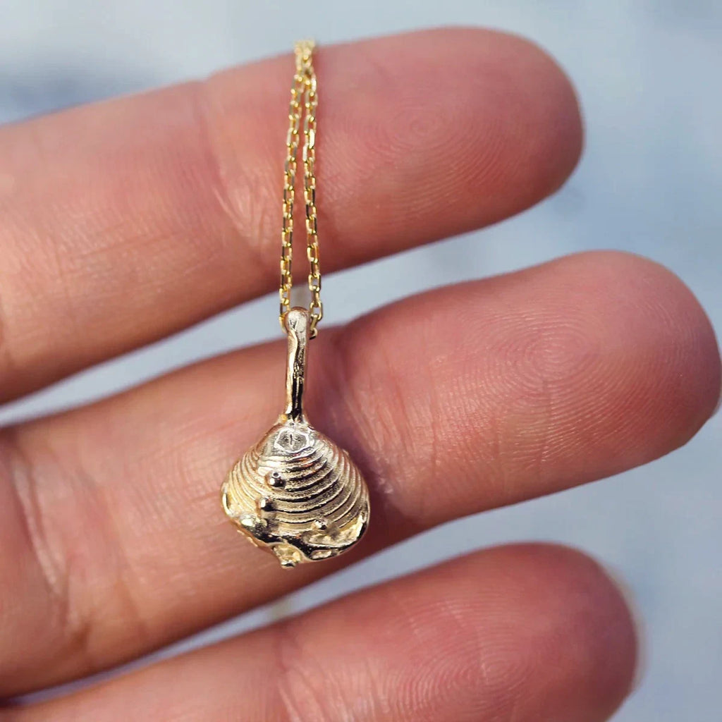 10k yellow gold pendant shaped like an organic shell, adorned with fine details and delicate gold beads, captured on a white background. Designed by Emma Glover, available at Ruby Mardi in Little Italy, Montreal.