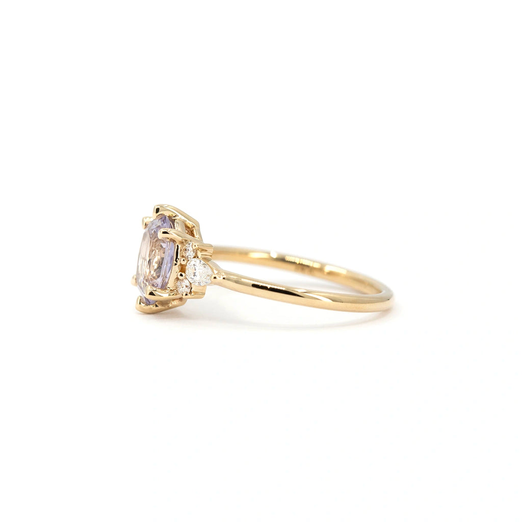 Side view of lilac sapphire ring with pear-shaped diamond accents, set in 14k yellow gold. Fine jewelry by Maksym Jewelry, available at Ruby Mardi in Montreal.