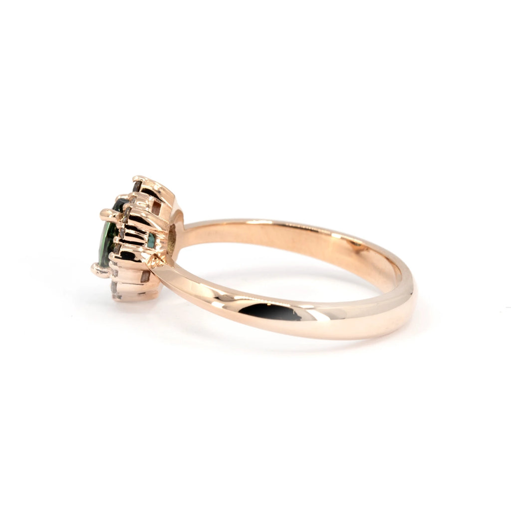 Side view of a rose gold engagement ring showcasing an oval teal sapphire and a pointed halo of brown and white diamonds. The setting reveals intricate prong details. Handcrafted by Ruby Mardi in Montreal.