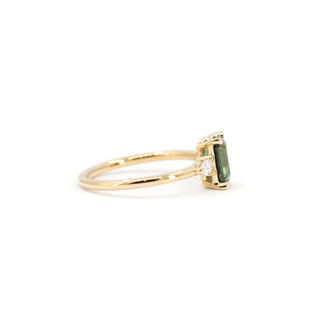 Side view of a yellow gold engagement ring featuring an emerald-cut green sapphire and pear-shaped diamond accents. Handmade by Maksym Jewelry in Montreal, available at Ruby Mardi.