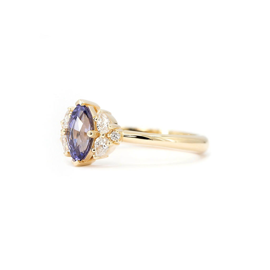 Side angle of a yellow gold engagement ring featuring a marquise purple sapphire with diamond clusters.