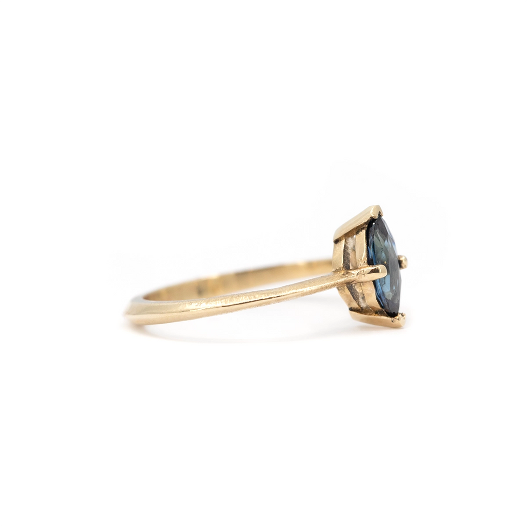 Side view of marquise blue sapphire solitaire ring with knife-edge yellow gold band and raw textured finish, minimalist fine jewelry by Ruby Mardi.