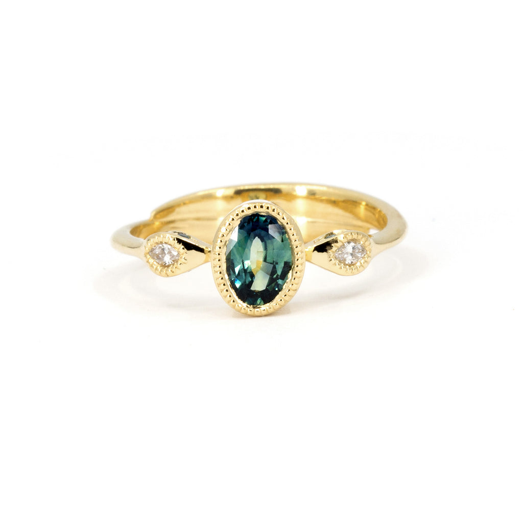 An absolutely unique yellow gold ring: the band is formed by two superimposed snakes that join a central oval green sapphire on either side, set in a closed setting with miligrain detail. The gold snakes have white diamond eyes on the front and green diamond eyes on the sides! This exceptional engagement ring is available only at Canada's coolest jewelry store, Ruby Mardi. It was made by Emily Gill.